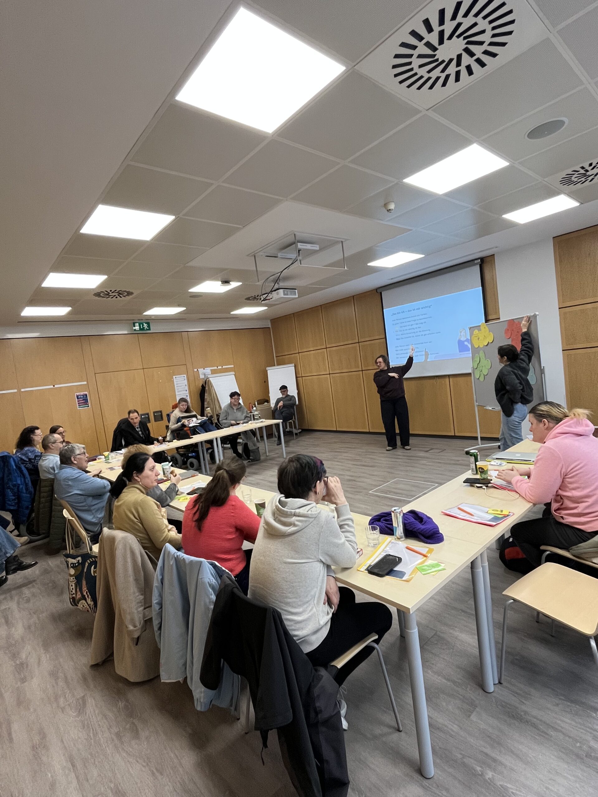 mesnchen sitzen an Tischen in U-Form und sehen nach vorne zu einer Vortragenden.